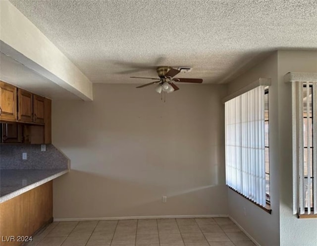 unfurnished dining area with ceiling fan, a textured ceiling, light tile patterned flooring, and a healthy amount of sunlight