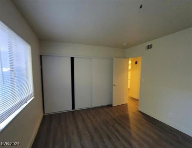 unfurnished bedroom with dark hardwood / wood-style floors, a closet, and multiple windows