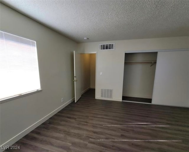 unfurnished bedroom featuring a textured ceiling, a closet, and dark wood-type flooring