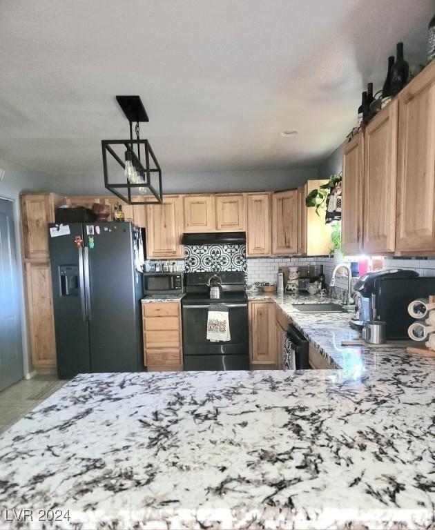 kitchen with light stone counters, tasteful backsplash, a sink, under cabinet range hood, and black appliances