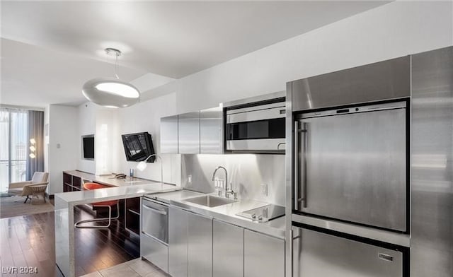 kitchen featuring sink, light wood-type flooring, tasteful backsplash, built in appliances, and hanging light fixtures