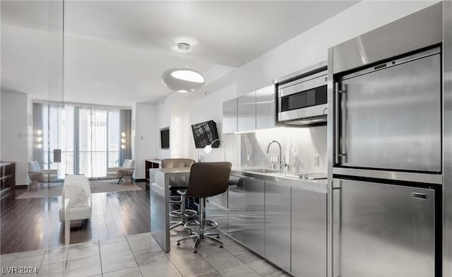 kitchen with sink, light wood-type flooring, white cabinets, built in appliances, and hanging light fixtures