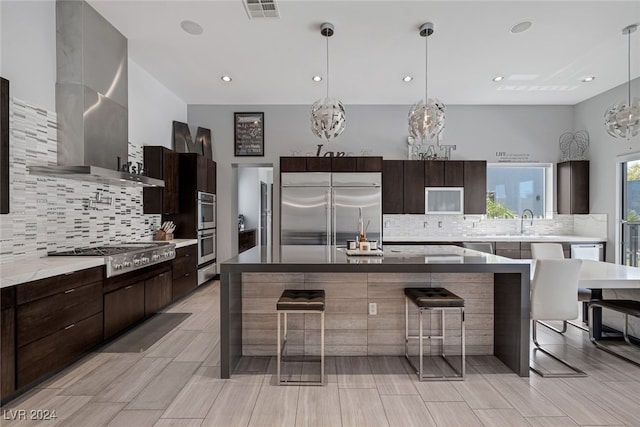 kitchen featuring a breakfast bar area, appliances with stainless steel finishes, wall chimney exhaust hood, and backsplash