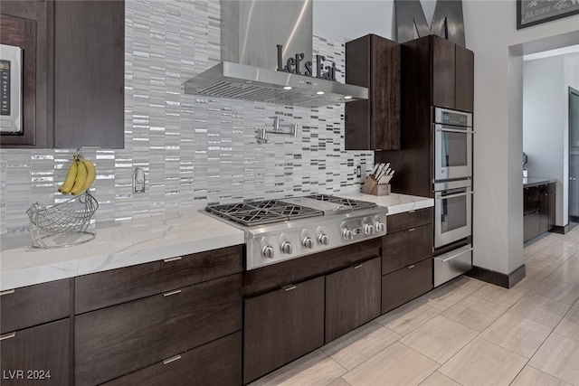 kitchen with wall chimney range hood, tasteful backsplash, appliances with stainless steel finishes, and dark brown cabinets