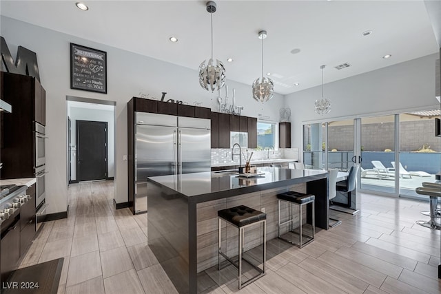 kitchen featuring decorative backsplash, pendant lighting, a kitchen island with sink, a kitchen bar, and built in fridge