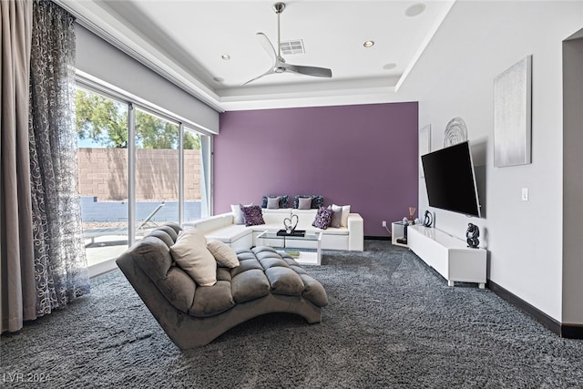 carpeted living room with ceiling fan and a tray ceiling