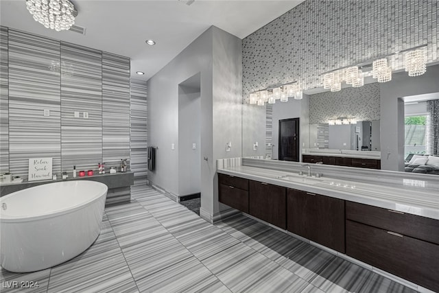 bathroom featuring an inviting chandelier, tile walls, tile patterned flooring, vanity, and a bathtub