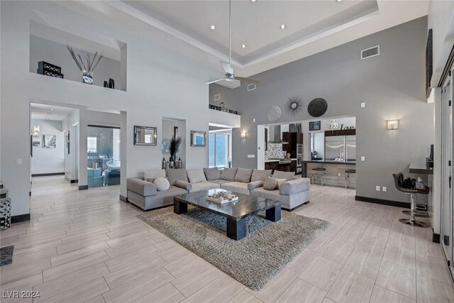 tiled living room featuring ceiling fan, a tray ceiling, and a towering ceiling