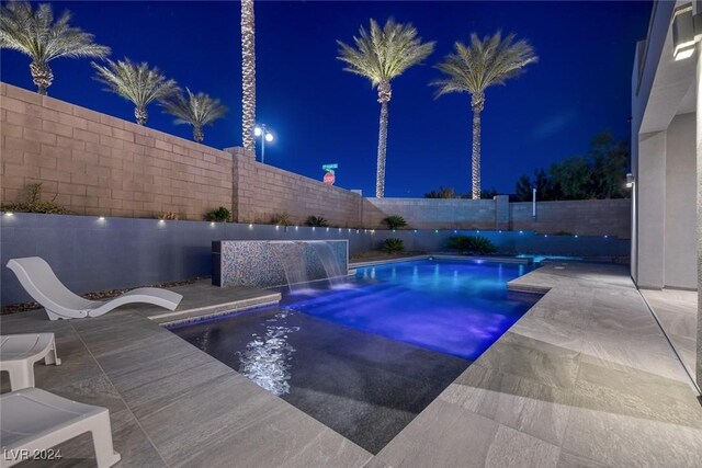 pool at twilight featuring pool water feature and a patio