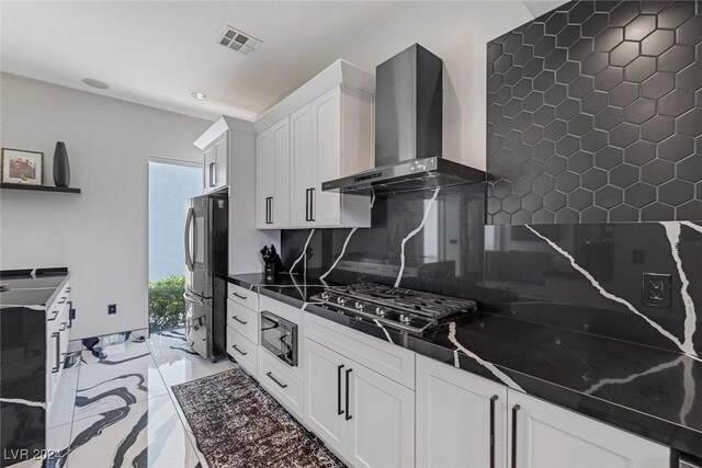 kitchen with wall chimney range hood, tasteful backsplash, white cabinetry, and appliances with stainless steel finishes