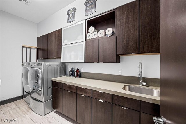 clothes washing area featuring sink, washing machine and dryer, light tile patterned flooring, and cabinets