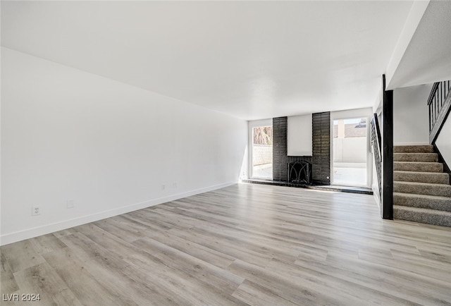 unfurnished living room featuring a fireplace, light hardwood / wood-style flooring, and brick wall