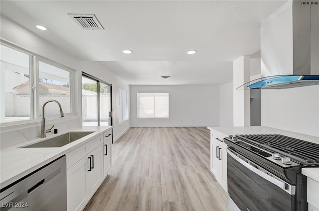 kitchen featuring sink, light wood-type flooring, wall chimney exhaust hood, stainless steel dishwasher, and white cabinets