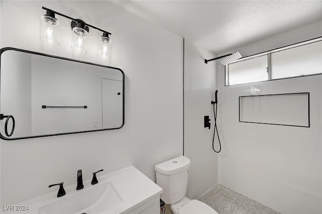 bathroom with a textured ceiling, vanity, tiled shower, and toilet