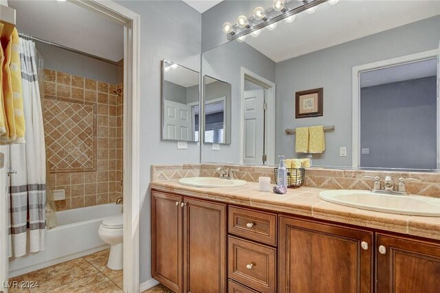 full bathroom featuring toilet, double sink vanity, shower / bath combo with shower curtain, and tile patterned flooring