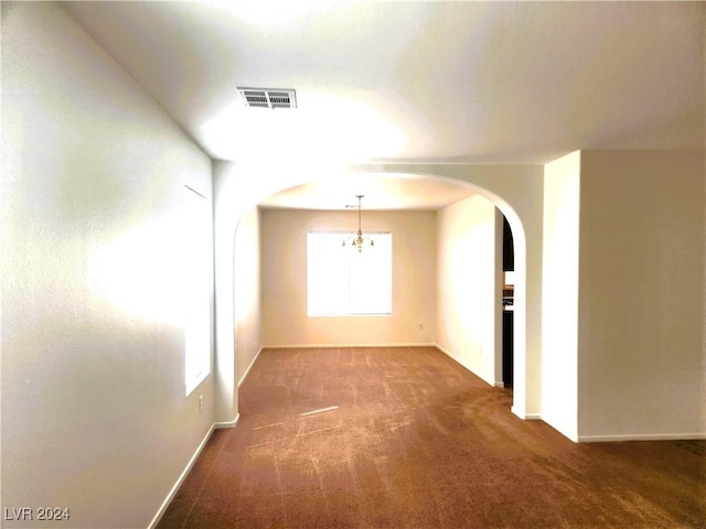 empty room featuring arched walkways, carpet, visible vents, a chandelier, and baseboards