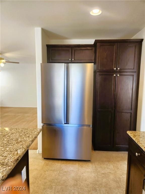 kitchen with dark brown cabinetry, a ceiling fan, light stone counters, freestanding refrigerator, and recessed lighting