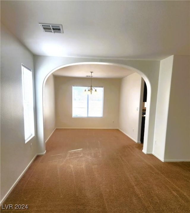 empty room featuring arched walkways, baseboards, visible vents, and carpet