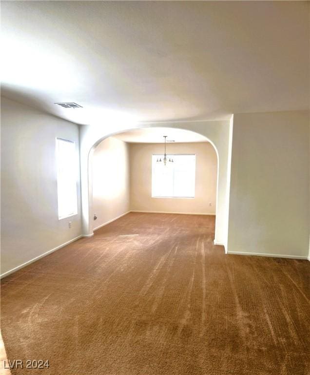 spare room featuring arched walkways, a chandelier, visible vents, baseboards, and carpet