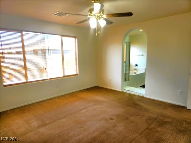 carpeted empty room with a ceiling fan, arched walkways, visible vents, and baseboards