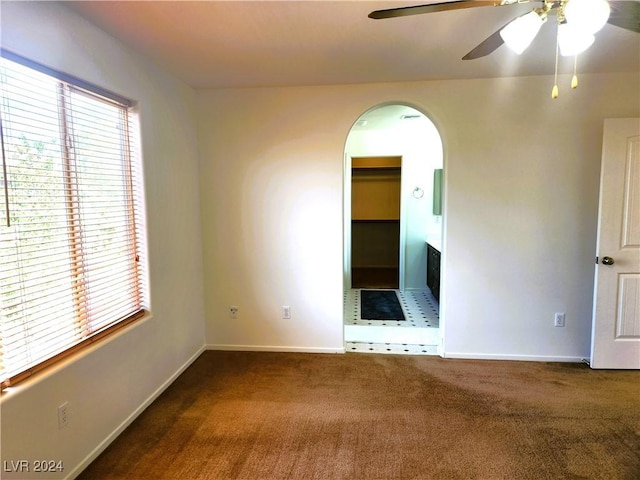 empty room featuring a ceiling fan, arched walkways, carpet flooring, and baseboards