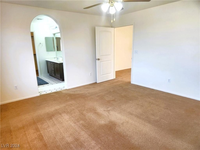 carpeted spare room featuring a ceiling fan, arched walkways, a sink, and baseboards