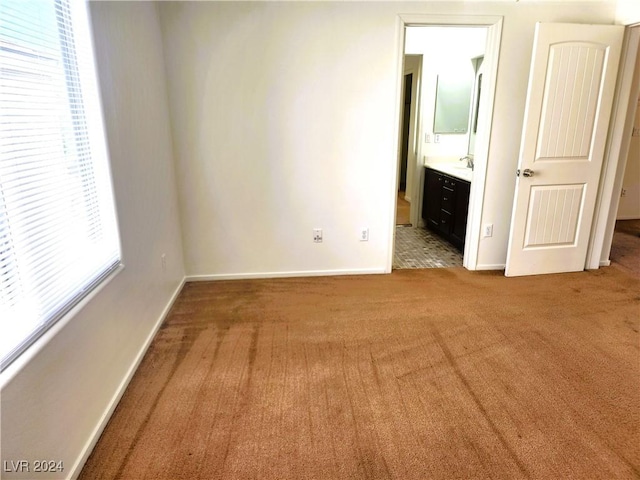 unfurnished bedroom featuring light carpet, baseboards, and ensuite bathroom