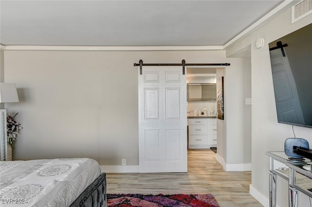 bedroom featuring a barn door, light hardwood / wood-style floors, and ornamental molding