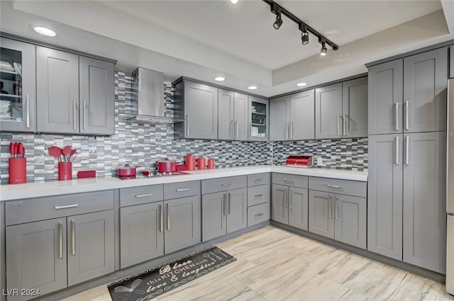 kitchen featuring gray cabinetry, stainless steel gas stovetop, track lighting, wall chimney exhaust hood, and decorative backsplash