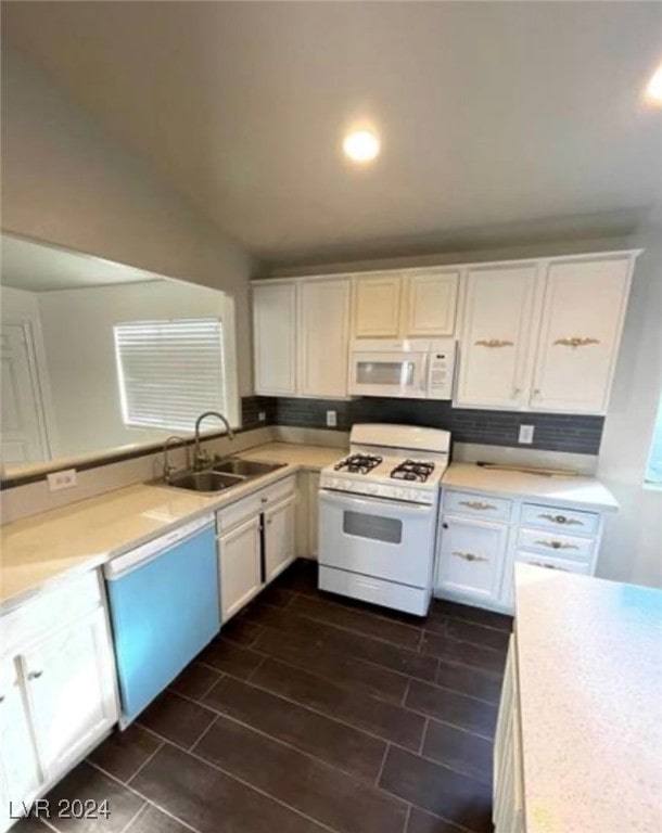 kitchen with sink, white appliances, vaulted ceiling, and white cabinetry