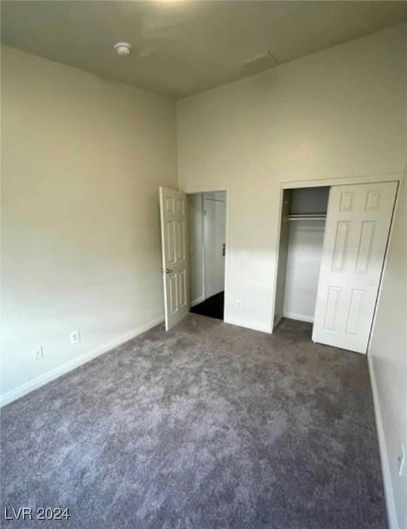 unfurnished bedroom featuring a closet, dark colored carpet, and a towering ceiling