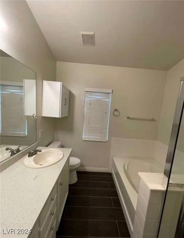 bathroom with tiled tub, tile patterned floors, vanity, and toilet