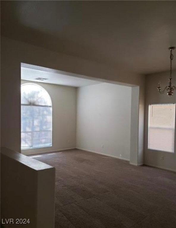 carpeted empty room featuring a chandelier