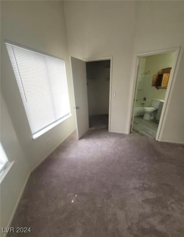 unfurnished bedroom featuring carpet, ensuite bath, and a towering ceiling