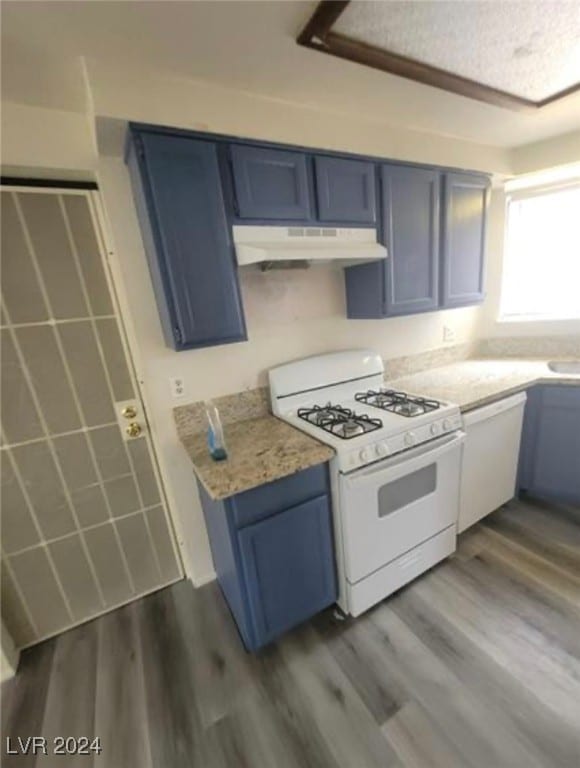 kitchen with blue cabinets, dark wood-type flooring, custom range hood, and white appliances