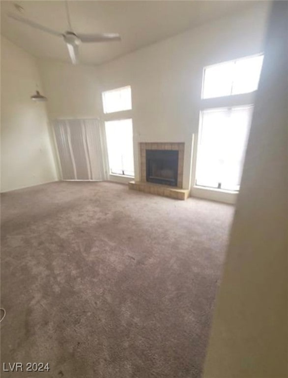 unfurnished living room featuring ceiling fan, a wealth of natural light, carpet flooring, and a fireplace