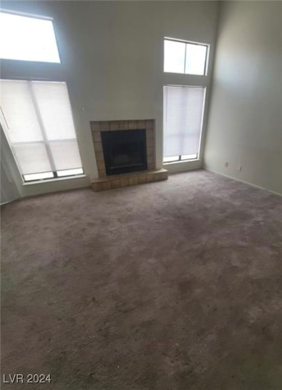 unfurnished living room featuring carpet flooring, a tiled fireplace, and a high ceiling