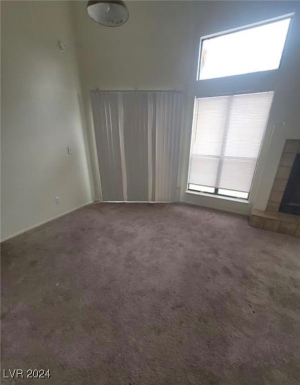 carpeted empty room featuring a high ceiling and a tile fireplace