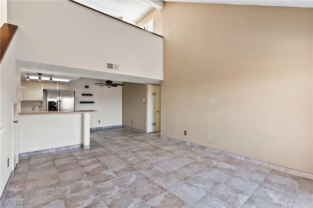 unfurnished living room featuring high vaulted ceiling, sink, ceiling fan, beam ceiling, and a barn door