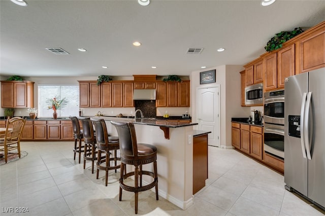 kitchen with dark stone counters, light tile patterned floors, a kitchen island with sink, and stainless steel appliances