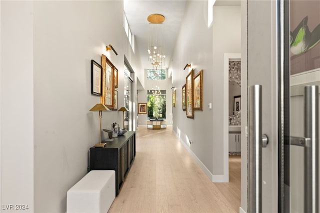 hallway featuring light hardwood / wood-style flooring, an inviting chandelier, and a towering ceiling