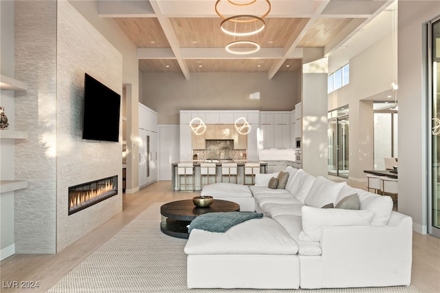 living room with a fireplace, beamed ceiling, light hardwood / wood-style flooring, wooden ceiling, and a towering ceiling