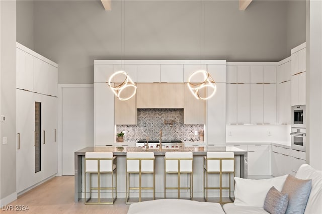 kitchen with sink, a high ceiling, an island with sink, and hanging light fixtures