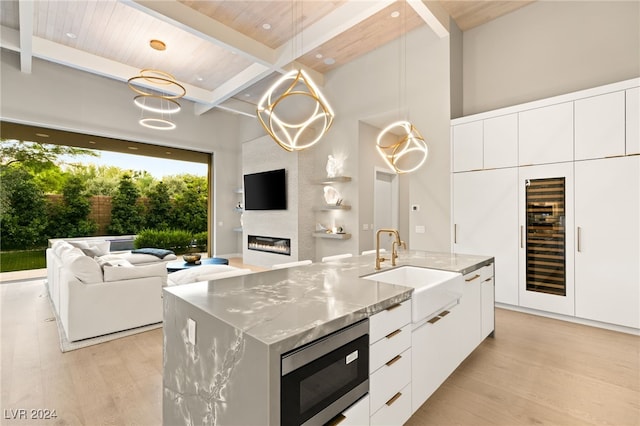 kitchen featuring wooden ceiling, an island with sink, beamed ceiling, and stainless steel microwave