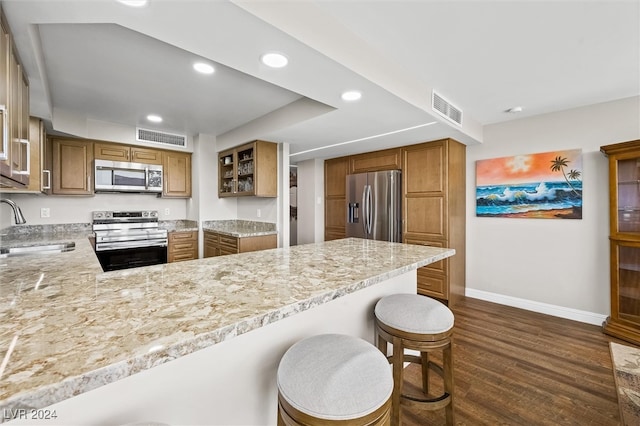 kitchen with stainless steel appliances, dark hardwood / wood-style flooring, kitchen peninsula, sink, and a breakfast bar area