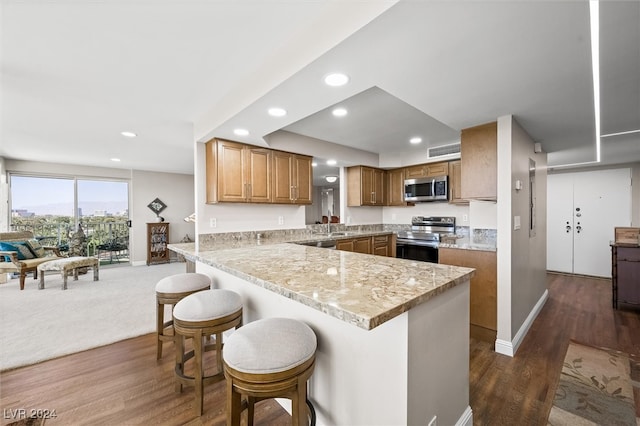 kitchen featuring light stone counters, kitchen peninsula, a breakfast bar area, dark hardwood / wood-style floors, and appliances with stainless steel finishes