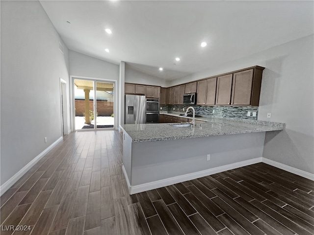 kitchen with dark hardwood / wood-style flooring, tasteful backsplash, vaulted ceiling, appliances with stainless steel finishes, and sink