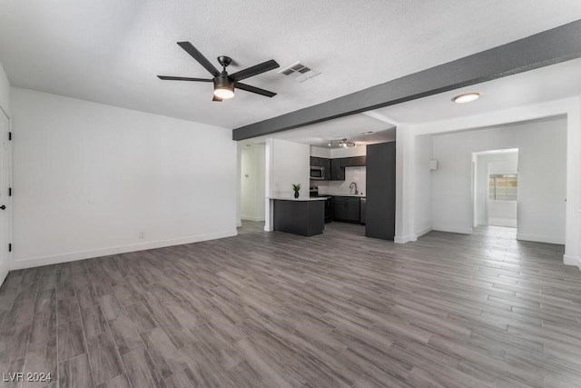 unfurnished living room featuring sink, ceiling fan, a textured ceiling, and hardwood / wood-style flooring