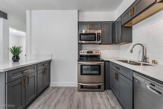 kitchen featuring appliances with stainless steel finishes, backsplash, sink, light wood-type flooring, and gray cabinetry