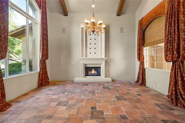 unfurnished living room with a fireplace, beam ceiling, light tile patterned flooring, and a chandelier